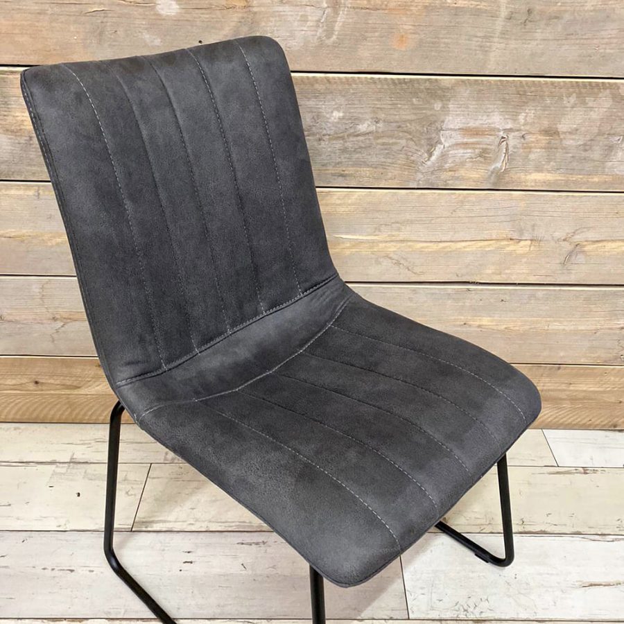 Anthrazitfarbener Stuhl aus mit Microfaserbezug und schwarzem Gestell vor einem hölzernen Hintergrund